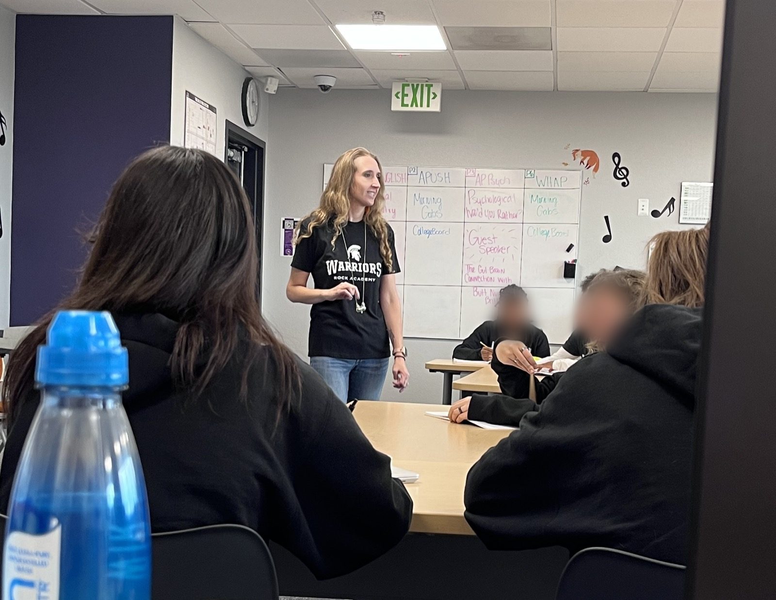 Taylor Fox teaching an AP class at the whiteboard, students seated around a shared table.